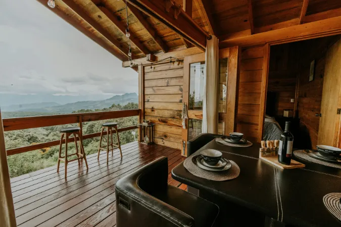 Airbnb: Chalé rústico com varanda e vista para montanhas. Mesa posta para refeições e decoração aconchegante.