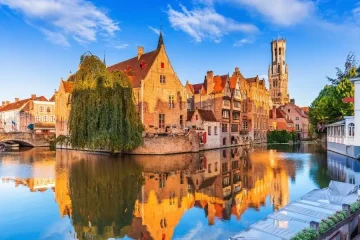 Bruges, Bélgica: arquitetura medieval refletida na água. Paisagem urbana, canais e torre histórica. Viagem, turismo.
