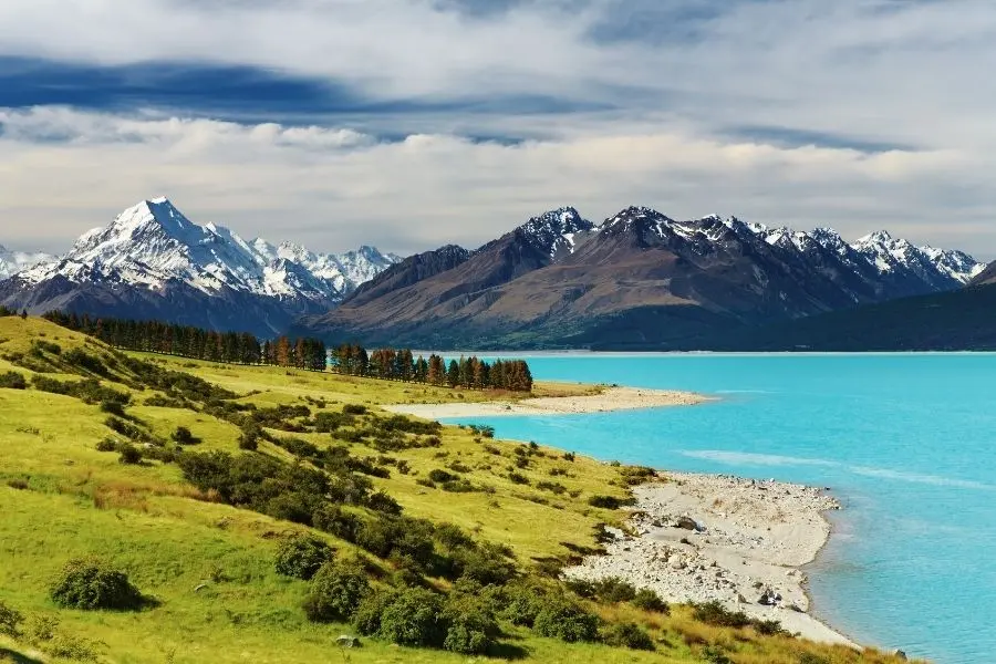 Paisagem épica da Nova Zelândia: lago azul turquesa, montanhas nevadas e colinas verdejantes. Aventura e cultura.
